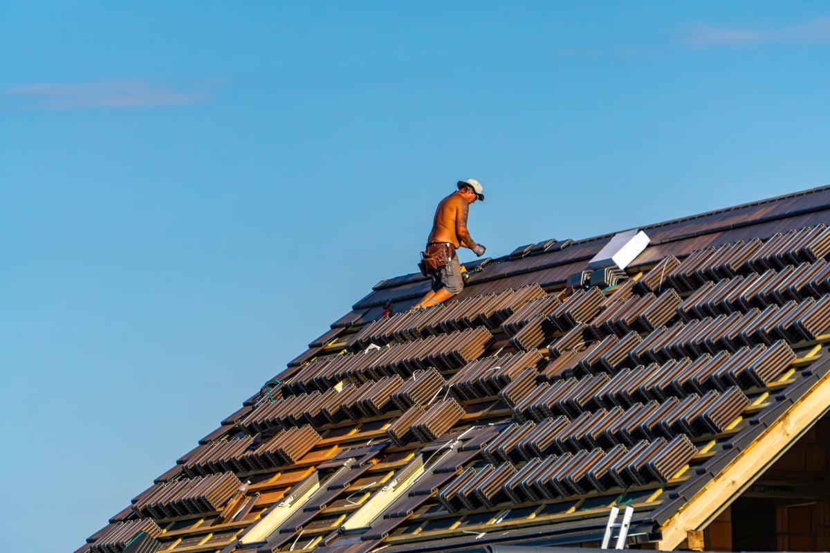 Sieroszewice,  Greater Poland Voivodeship, Poland - july 23, 2025 A roofer working on a roof installs metal sheeting on a sunny day. Professional roofing job under clear blue sky.