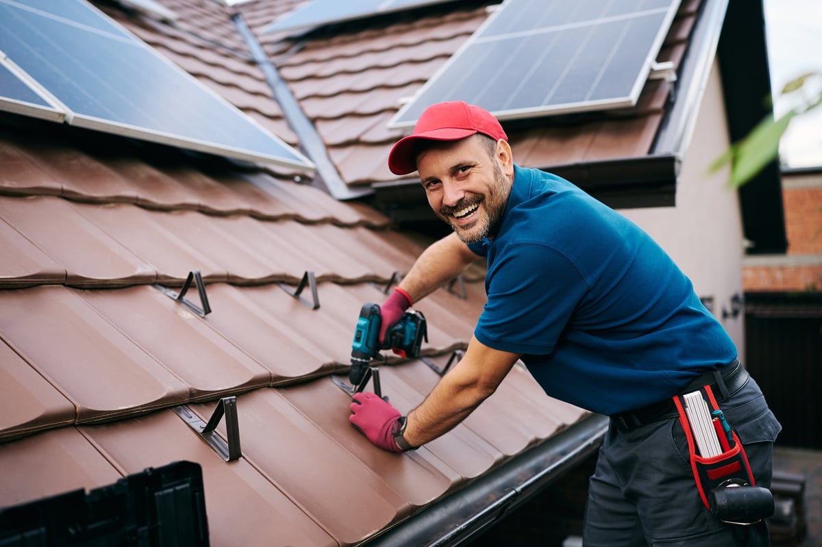 Happy worker installing snow guards on the roof top tiles and looking at camera. Copy space.