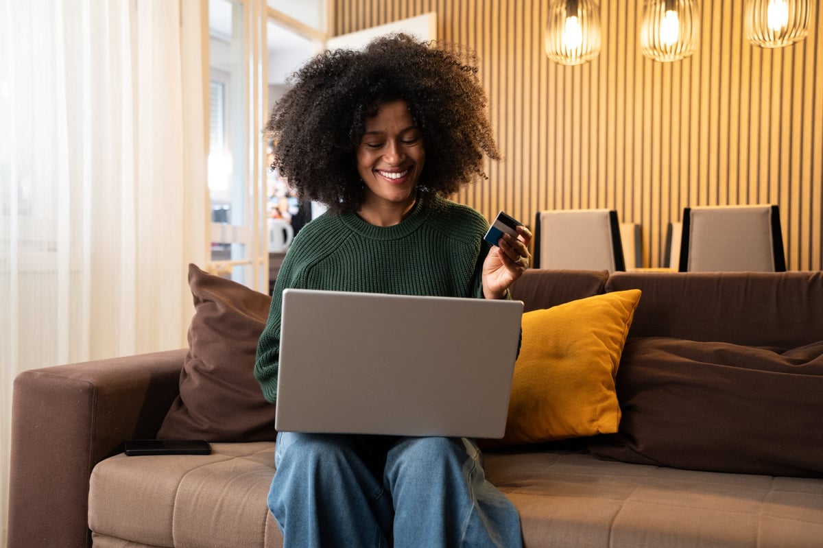Smiling woman shopping online at home using laptop and holding a credit card